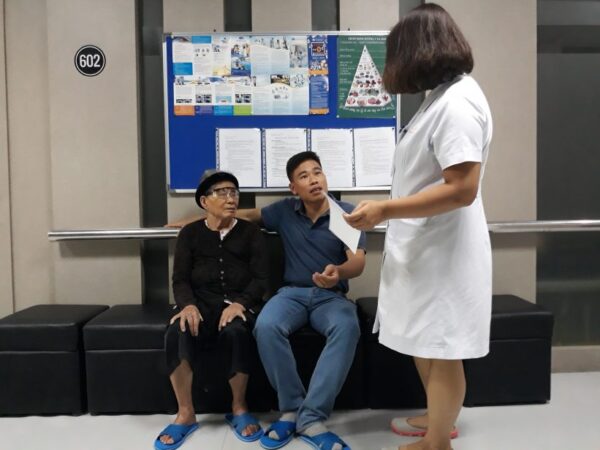 Patient Le Thi Sao (Mr. Ngoc’s mother) was inquired by the doctor while waiting for a follow-up examination 